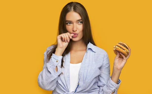 Fille affamée tenant un hamburger debout sur fond jaune — Photo