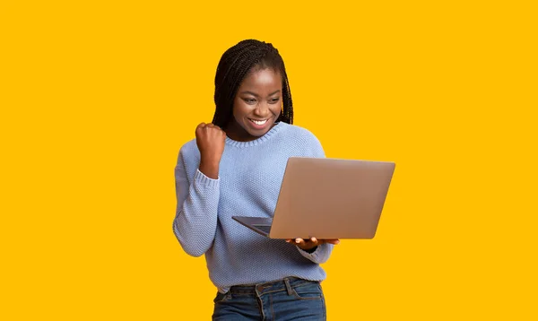 Successful black girl with laptop celebrating win over yellow background — Stock Photo, Image
