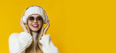 Çekici sarışın kadın sarı arka planda müzik dinliyor.