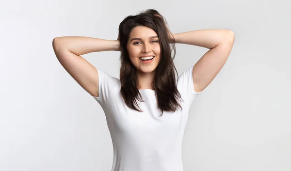 Ragazza positiva toccando capelli in piedi in posa su sfondo bianco, Studio — Foto Stock