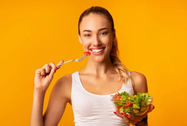 Menina desportiva desfrutando de salada vegetal de pé segurando tigela no estúdio — Fotografia de Stock