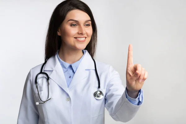 Médico sorridente tocando invisível Touchscreen em pé no estúdio, profundidade rasa — Fotografia de Stock