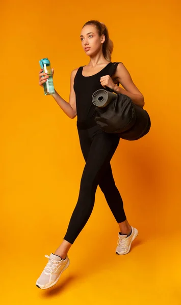 Mulher desportiva vai ao ginásio levando saco de fitness, fundo amarelo — Fotografia de Stock