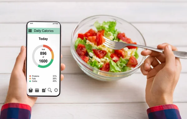 Ο άνθρωπος τρώει σαλάτα λαχανικών και καταμέτρηση θερμίδων σε mobile εφαρμογή — Φωτογραφία Αρχείου