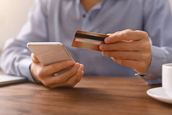 Ο άνθρωπος ψώνια σε απευθείας σύνδεση με πιστωτική κάρτα και smartphone στο χώρο εργασίας — Φωτογραφία Αρχείου