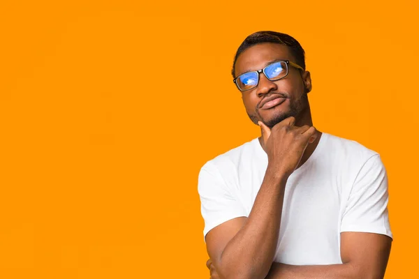 Ragazzo afro-americano pensare toccando mento in piedi su sfondo arancione — Foto Stock