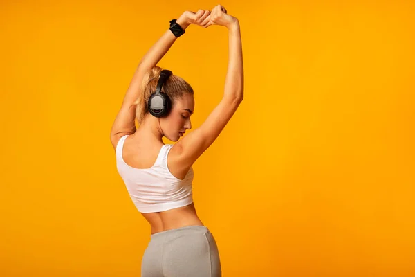 Αγνώριστη γυναίκα σε ακουστικά κάνει ασκήσεις τεντώματος, κίτρινο φόντο — Φωτογραφία Αρχείου