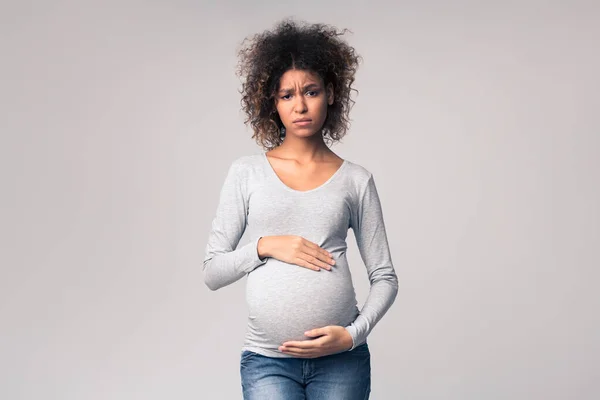 Fatiguée femme enceinte embrassant son ventre, fond gris — Photo