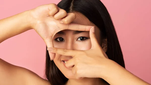 Азиатка смотрит сквозь рамку пальцами — стоковое фото