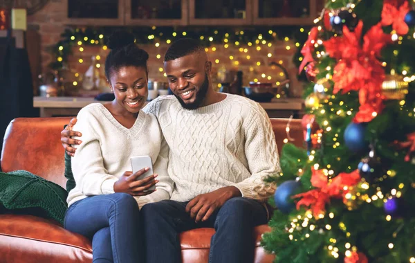 Usmívající se černý pár pomocí smartphone doma čtení vánoční přání — Stock fotografie