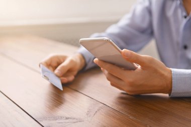 Elinde akıllı telefon ve kredi kartı olan tanınmayan bir adam internette ödeme yapıyor.