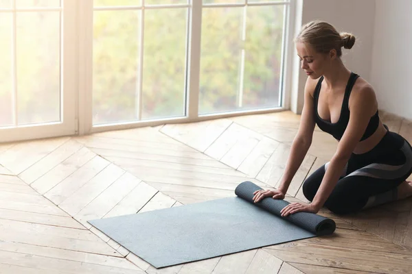 Atletica giovane donna rotolamento suo tappetino yoga dopo la meditazione — Foto Stock