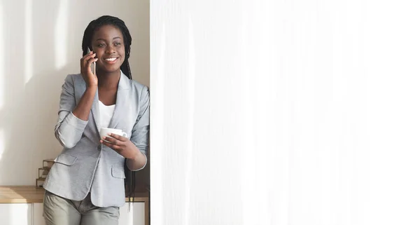 Черная деловая женщина разговаривает по мобильному телефону у окна в офисе — стоковое фото