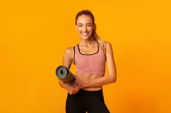 Chica sosteniendo la alfombra de fitness mirando a la cámara de pie, Studio Shot —  Fotos de Stock