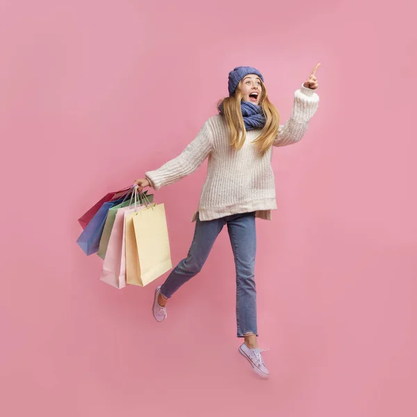 Menina de inverno emocional com compras apontando para algum lugar à parte — Fotografia de Stock