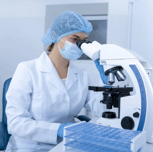 Trabajador de laboratorio con microscopio moderno en máscara y guantes —  Fotos de Stock