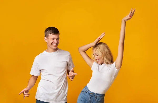 Feliz jovem casal dançando juntos sobre fundo amarelo no estúdio — Fotografia de Stock