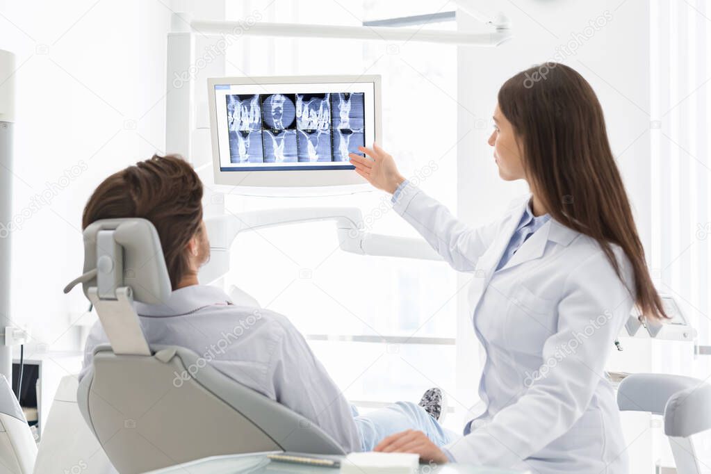 Pretty female dentist explaining her patient in chair x-ray results