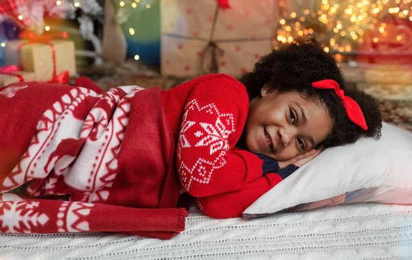 Милая маленькая афро-девочка, лежащая возле рождественской елки, ждет Санту — стоковое фото
