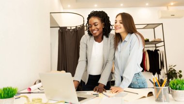 Two Diverse Tailors Using Laptop Working On Clothing Collection Indoor