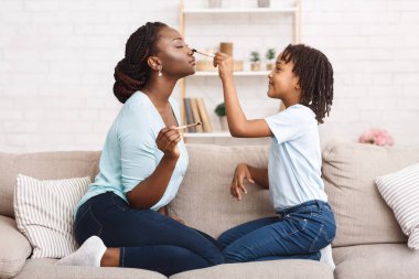 Küçük afro kız annesine makyaj yapıyor.