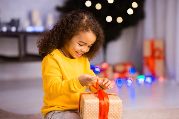 Curiosa niña negra abriendo caja de regalo en Nochebuena —  Fotos de Stock