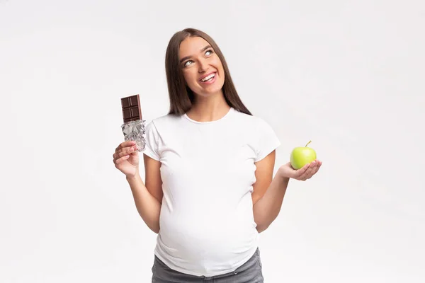 妊娠中の女の子チョコレートとアップルスタンドの間で選択,グレーの背景 — ストック写真