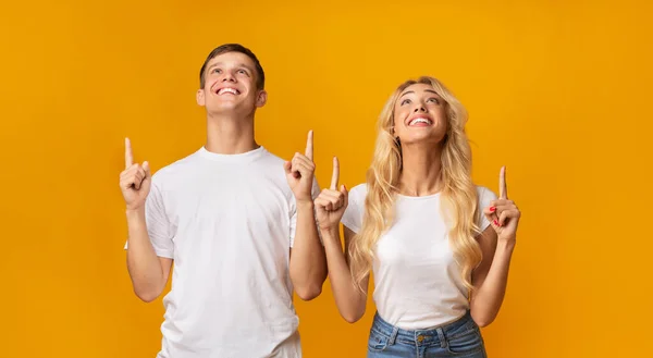 Smiling guy and girl looking and pointing upwards at copyspace — Stock Photo, Image