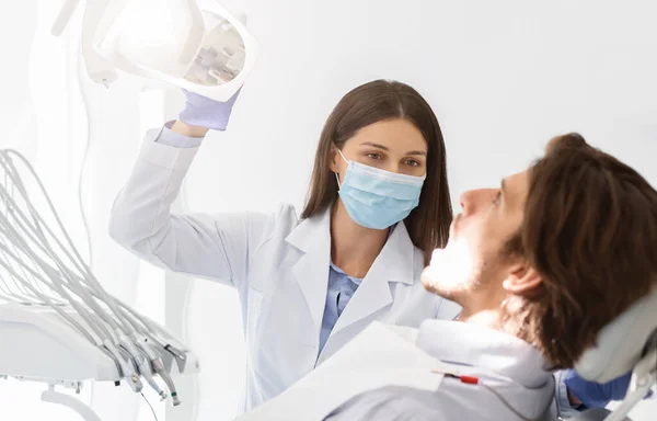 Tandarts in masker aan te zetten lamp voor het maken van check-up — Stockfoto