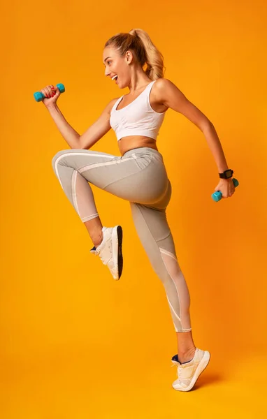 Garota excitada pulando segurando halteres se exercitando no estúdio, comprimento total — Fotografia de Stock