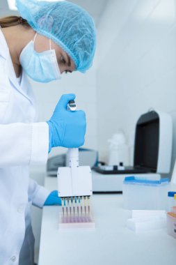 Genç bilim kadını test tüplerine kırmızı örnekler bırakıyor.