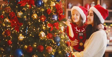Neşeli küçük kız annesiyle birlikte Noel ağacı ışıklarının tadını çıkarıyor.