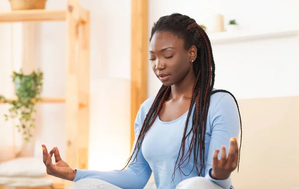 Молодая черная женщина медитирует в позе лотоса в постели в помещении — стоковое фото