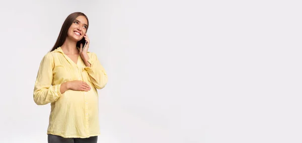 Беременная женщина разговаривает по мобильному телефону стоя на сером фоне, Панорама — стоковое фото