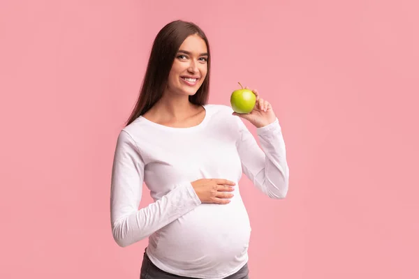 Zwangere vrouw met groene appel staande over roze achtergrond, Studio — Stockfoto