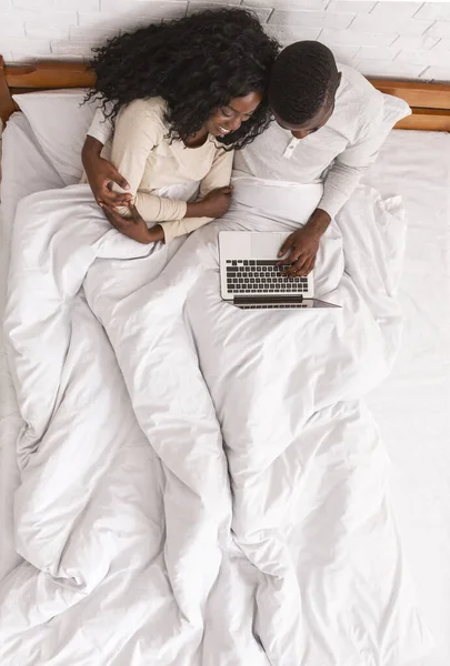 Afro ζευγάρι κάθεται στο κρεβάτι με φορητό υπολογιστή, top view — Φωτογραφία Αρχείου