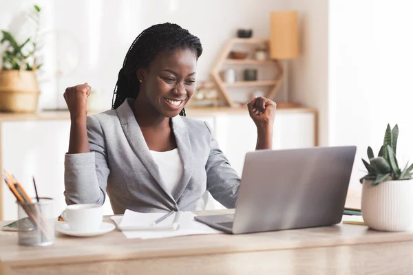 Emocionada mujer de negocios afro celebrando el éxito en el lugar de trabajo en la oficina moderna —  Fotos de Stock