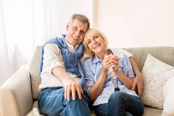Happy mature couple sitting on sofa and embracing — Stock Photo, Image