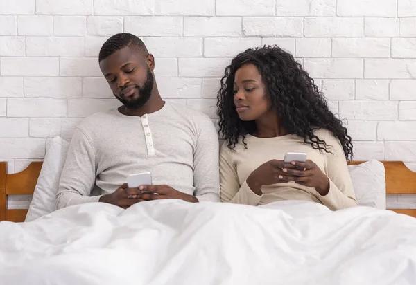 Jealous man peeking into wifes cellphone sitting on bed together — Stock Photo, Image