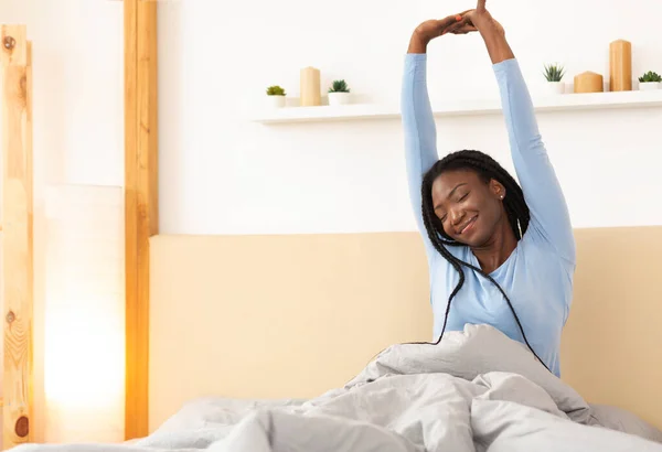 Alegre afro dama estiramiento levantamiento brazos sentado en cama —  Fotos de Stock