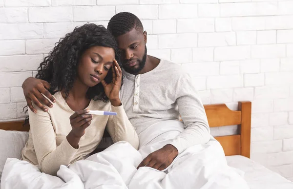 Casal preto sentado na cama com resultado negativo do teste de gravidez — Fotografia de Stock