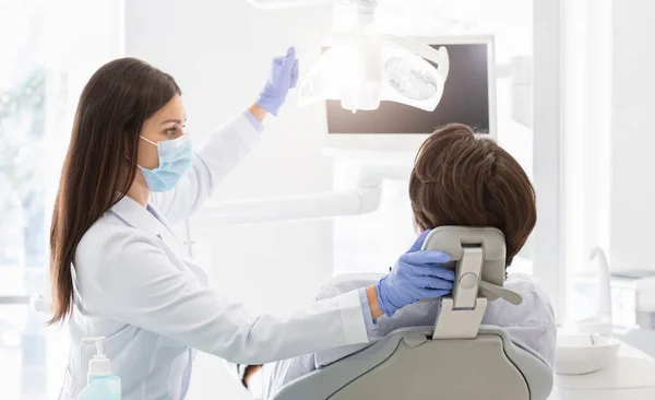 Médico dentista ligando a lâmpada antes de tratar o paciente — Fotografia de Stock