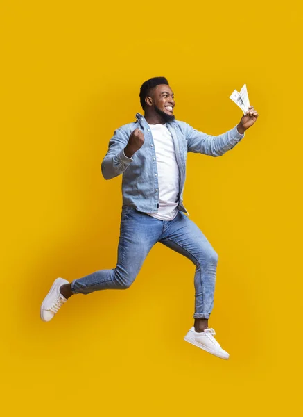 Euphoric afro man jumping with cash in hand over yellow background — Stock Photo, Image