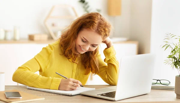 Horario de negocios. Chica sonriente tomando notas cerca de la computadora portátil — Foto de Stock