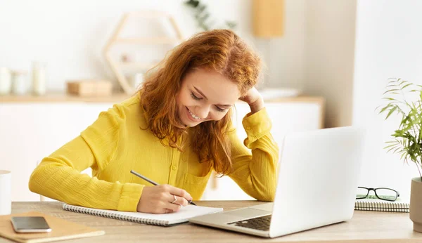 Calendrier des travaux. Souriante fille prenant des notes près de l'ordinateur portable — Photo