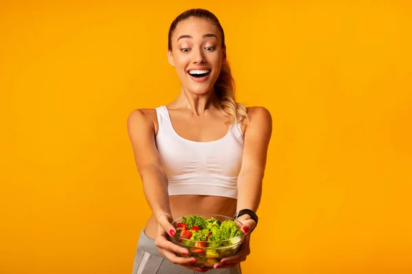 Mulher magro excitado segurando salada vegetal em pé no fundo amarelo — Fotografia de Stock