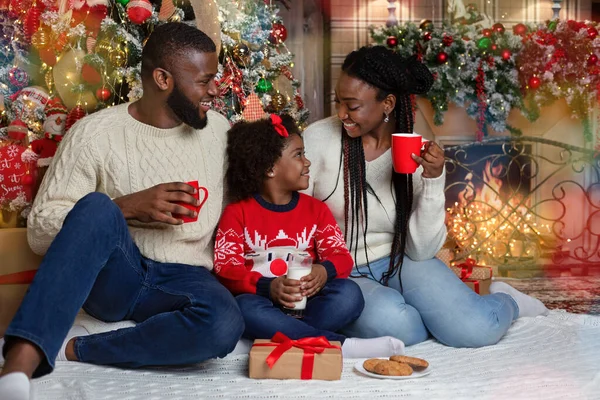 Joyful afro family drinking milk and eating cookies, celebrating Christmas together