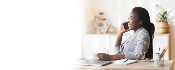 Entspannte schwarze Geschäftsfrau hält Tasse in der Hand und telefoniert am Arbeitsplatz — Stockfoto