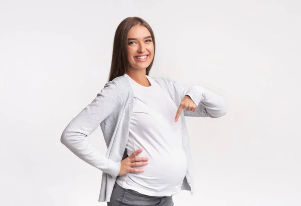 Těhotná dívka ukazující prst na břicho pózování přes bílé pozadí — Stock fotografie
