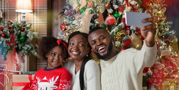 Feliz família negra de três tomando selfie perto da árvore de Natal — Fotografia de Stock